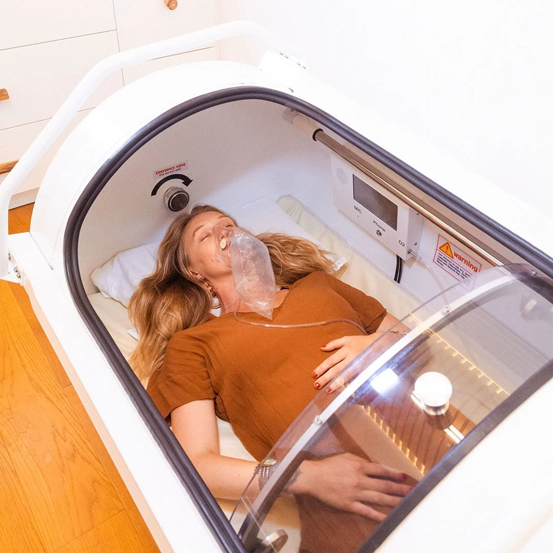Woman lying inside a hyperbaric oxygen chamber with a mask on her face.