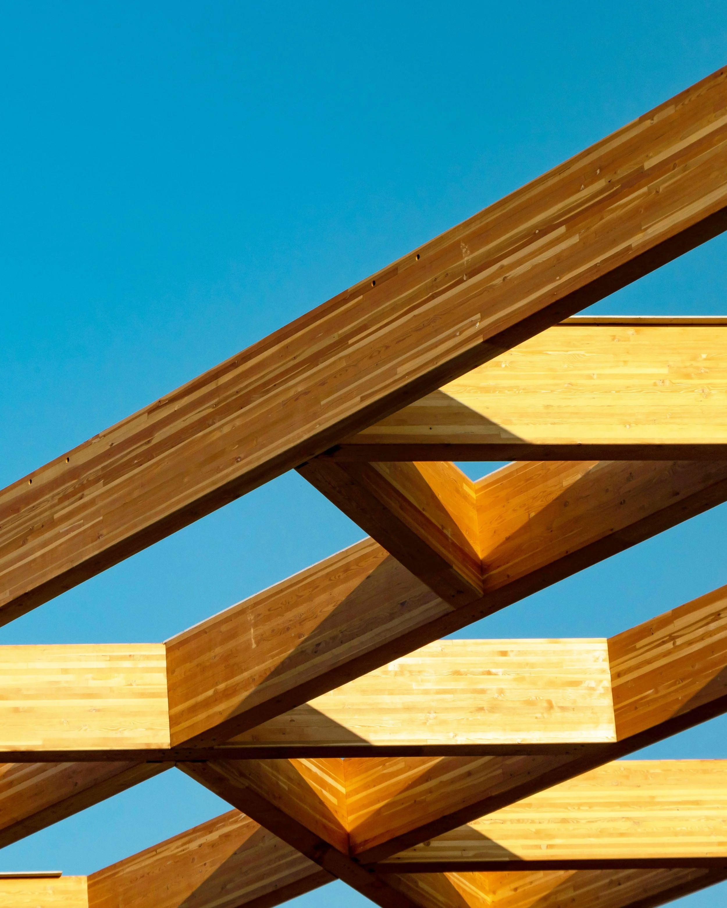 Close-up view of wooden beams and structural framework against a clear blue sky, showing geometric angles and patterns.