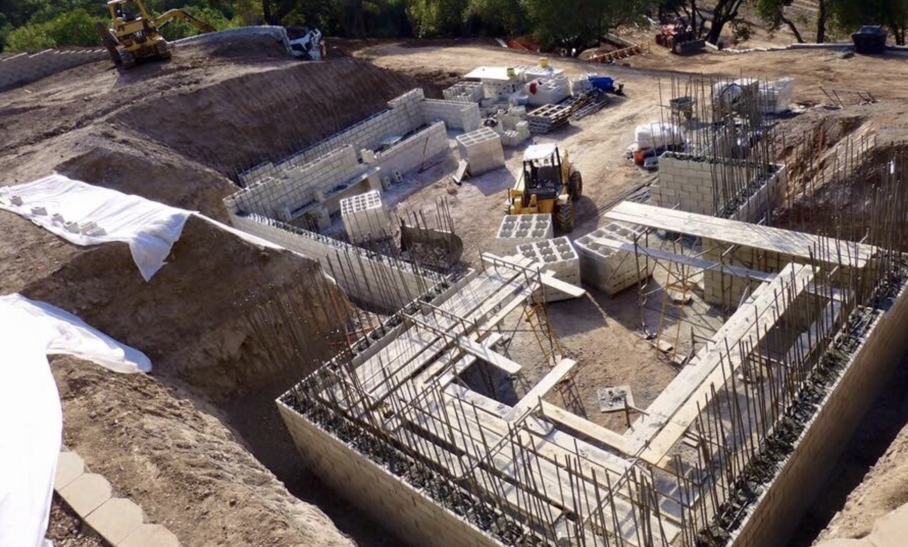 Underground construction site with concrete walls being built, reinforced with steel rebar, and construction equipment visible.