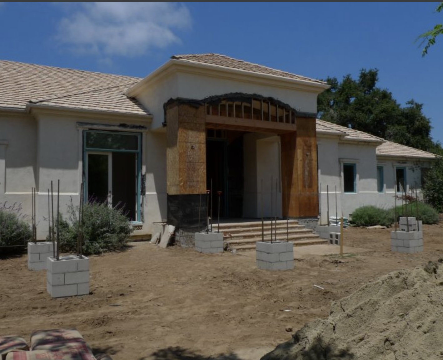 A house under construction with a new front porch, steps, and landscaping in progress, on a sunny day with a blue sky.