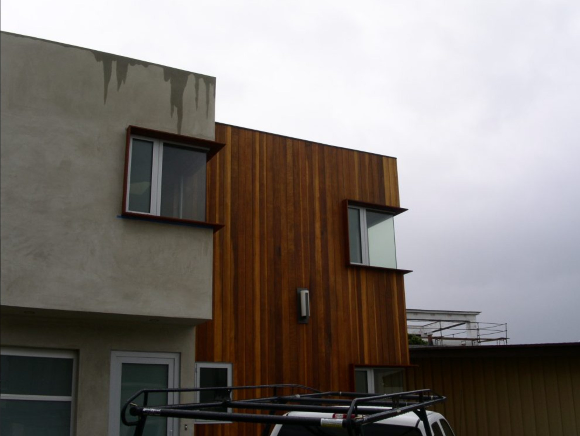 Modern building with a combination of concrete and wooden exterior, featuring rectangular windows and a flat roof, under an overcast sky.