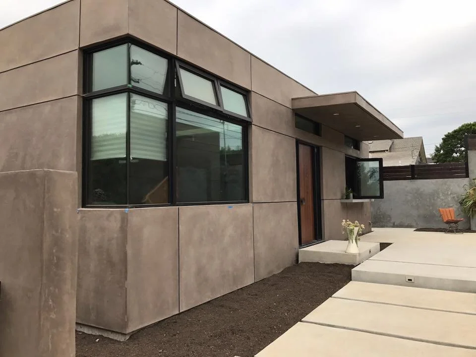 Modern house with large windows, a concrete pathway, and a small outdoor seating area with an orange chair.