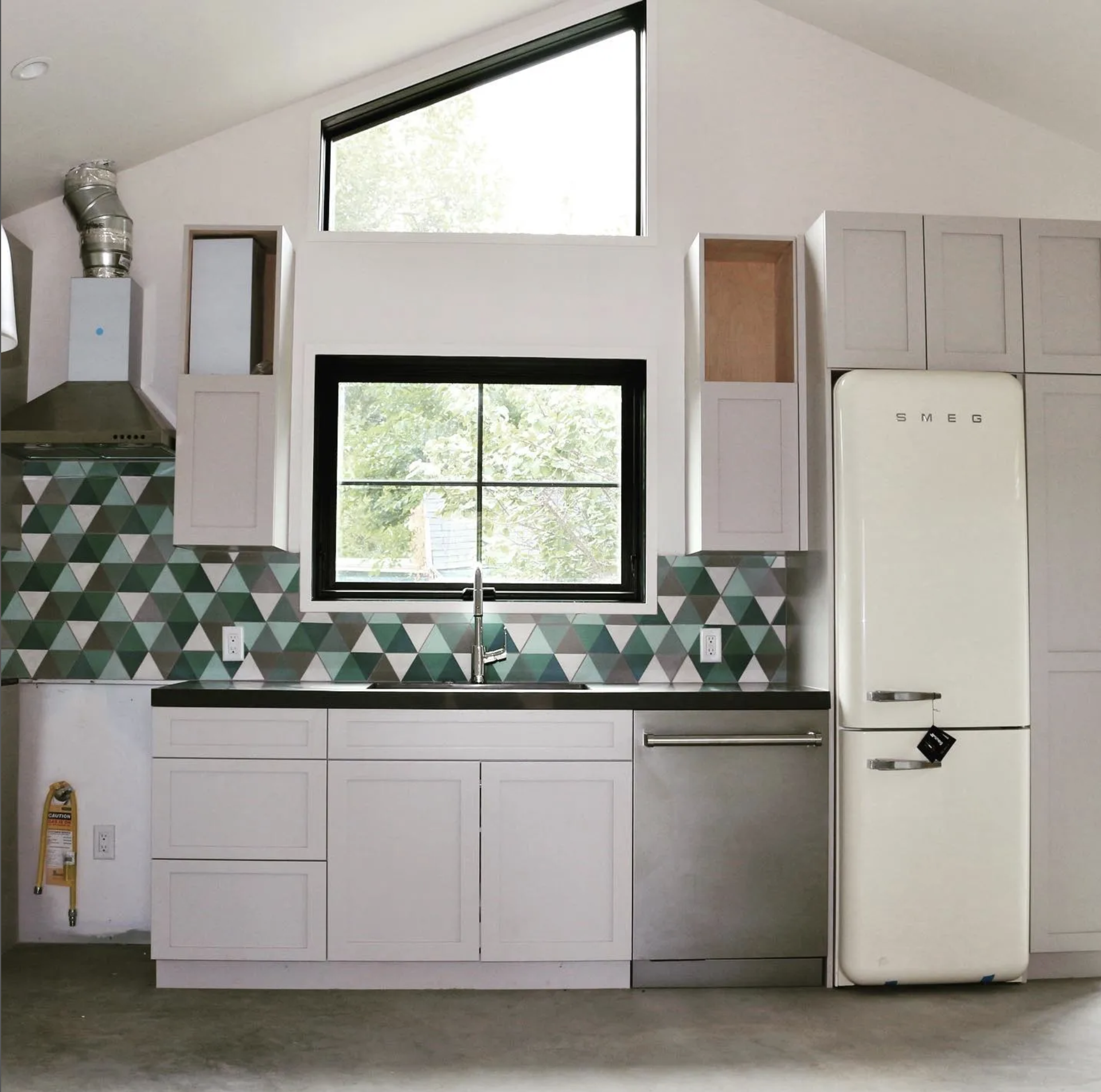 Modern kitchen with white cabinets, a geometric backsplash, a Smeg refrigerator, and a large window above the sink.
