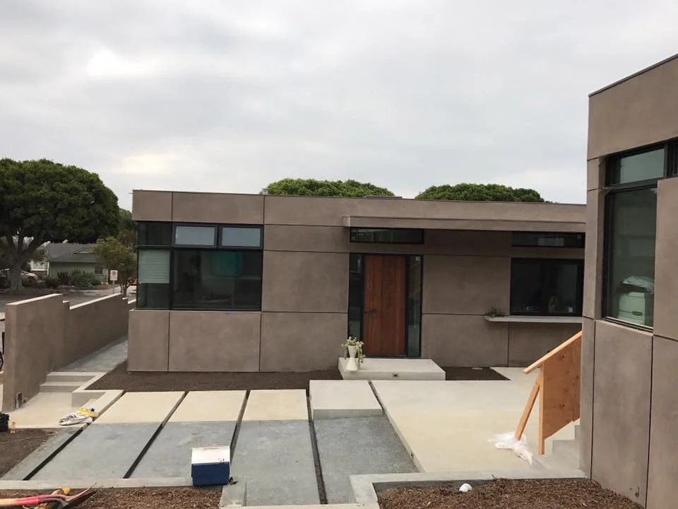 Exterior of a modern house under construction with a concrete pathway and a wooden front door.