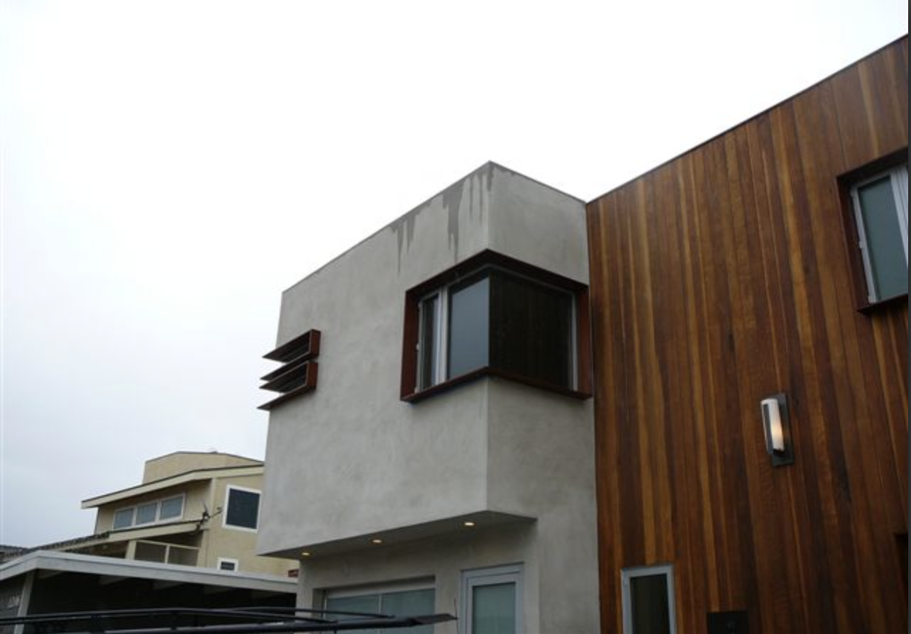 Modern building with a concrete and wooden exterior, featuring a bay window and a wall-mounted light fixture.