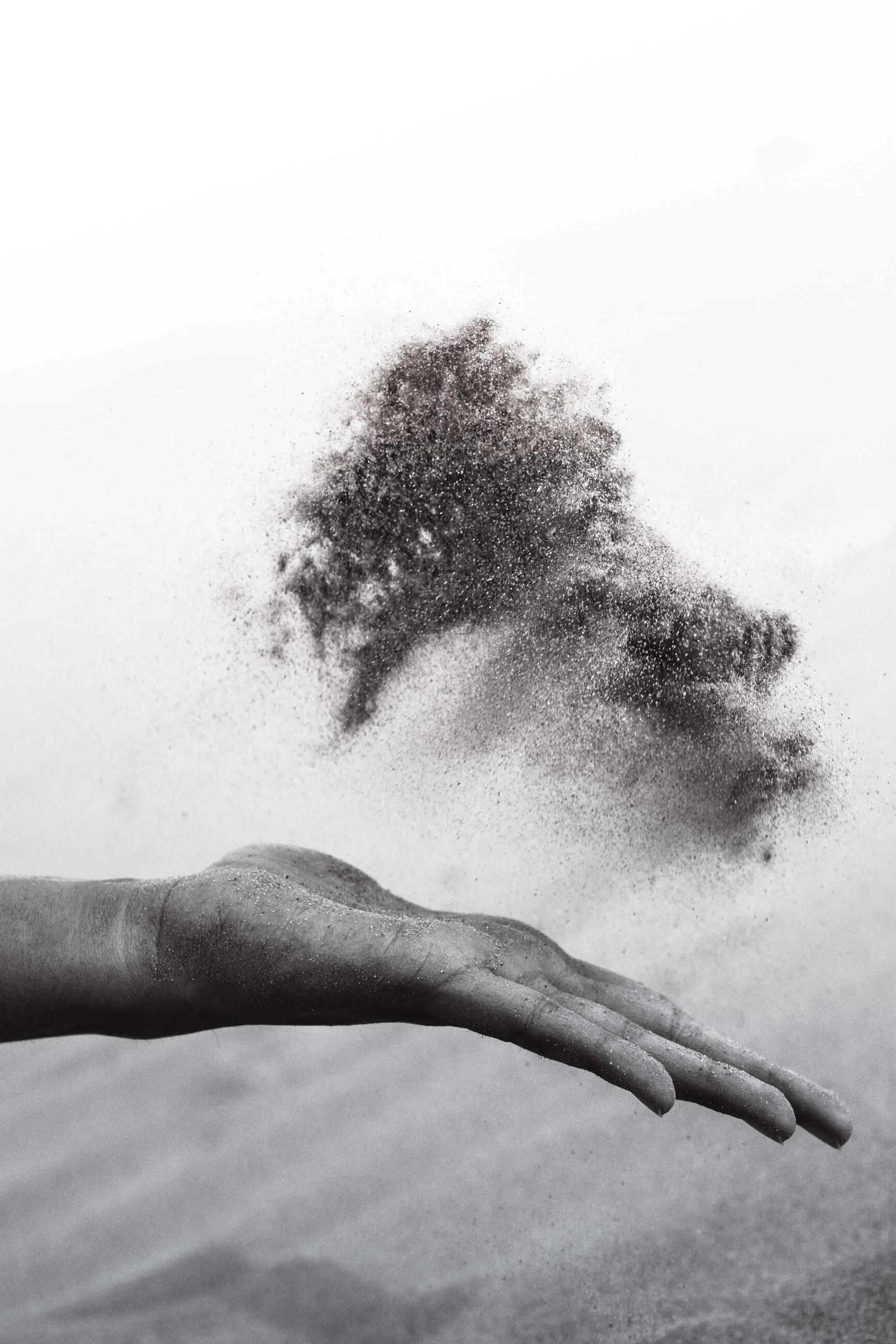 A hand with sand on it, tossing sand into the air against a plain background.