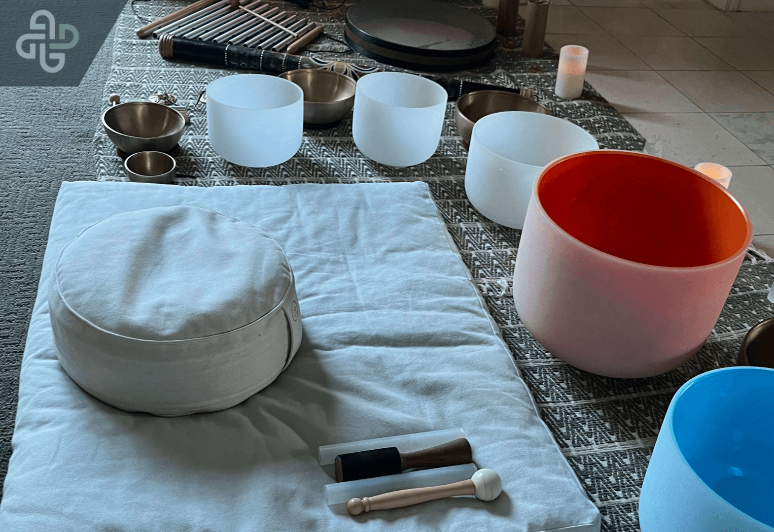 Crystal singing bowls, Tibetan singing bowls, chimes, and meditation cushions arranged on a wellness mat for a peaceful sound healing and mindfulness session.