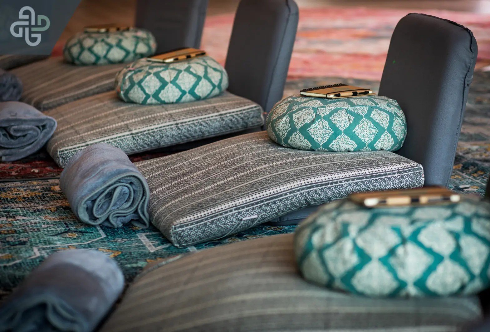 Spa-style massage mats with teal-and-white patterned cushions and rolled gray towels arranged on woven rugs, creating a calm, inviting scene.