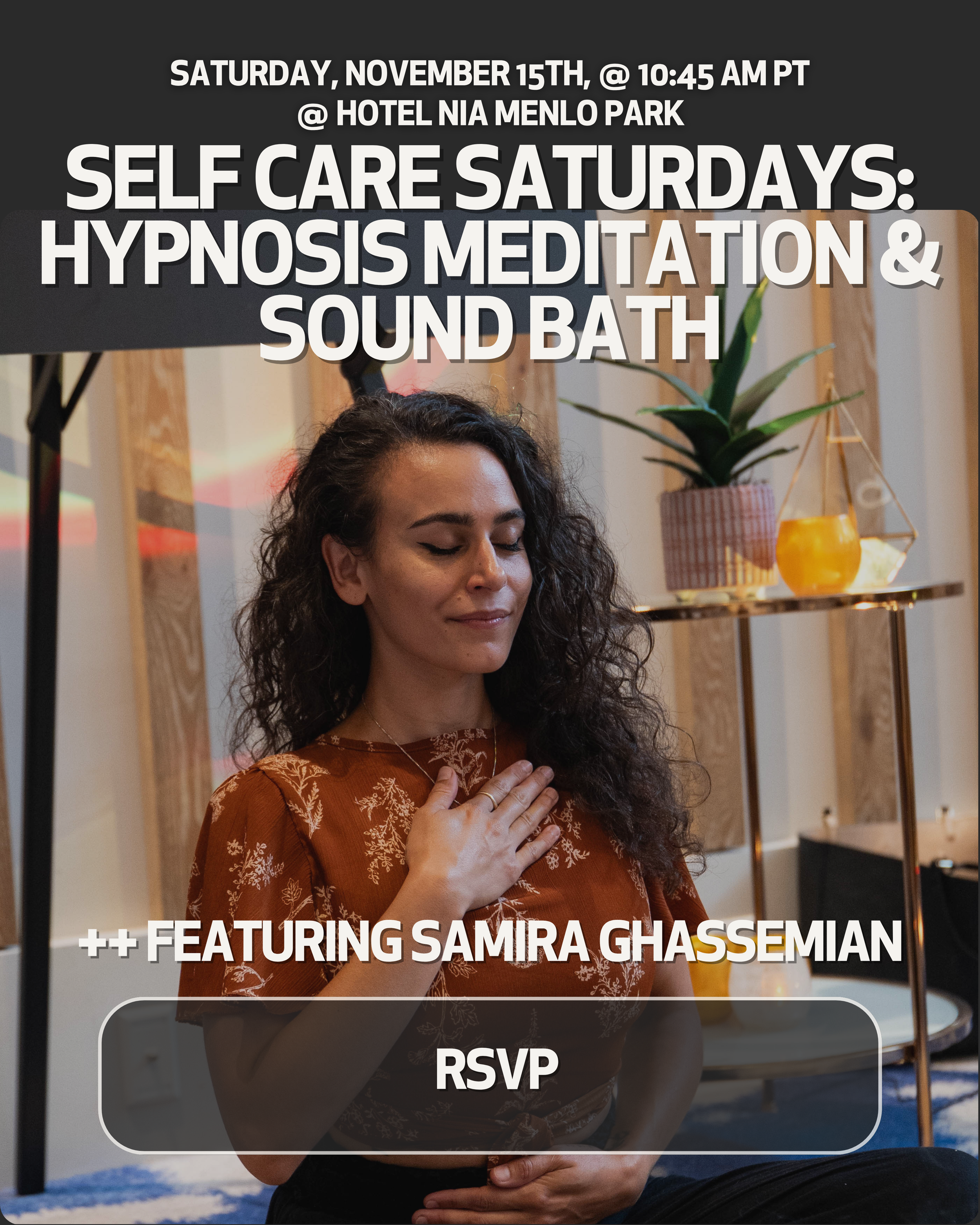 A woman with curly hair sitting cross-legged on the floor with her eyes closed, hands on her chest in a yoga or meditation pose, in a cozy indoor setting with plants and warm lighting.