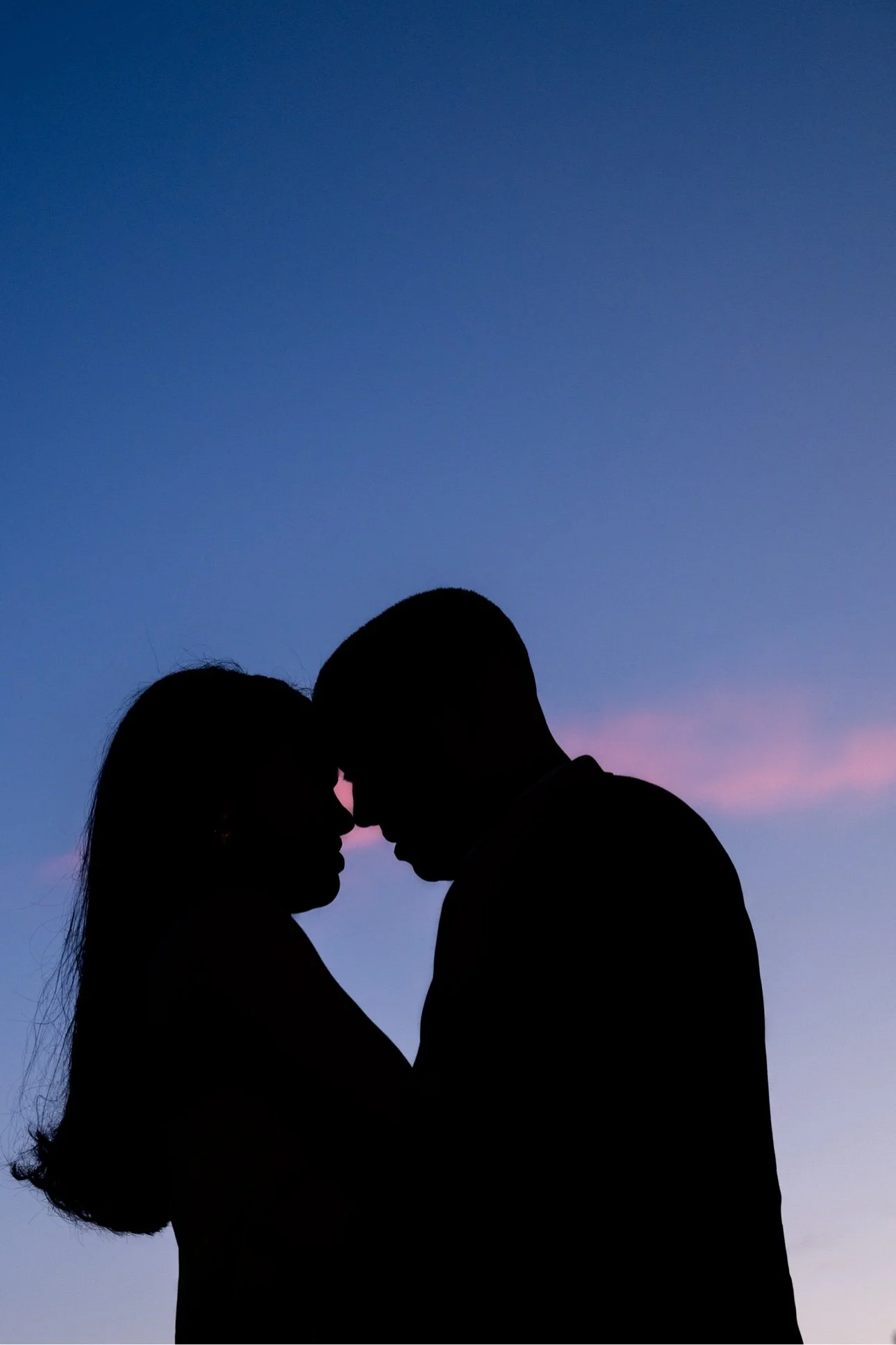 Silhouette of a couple touching foreheads against a colorful sunset sky.
