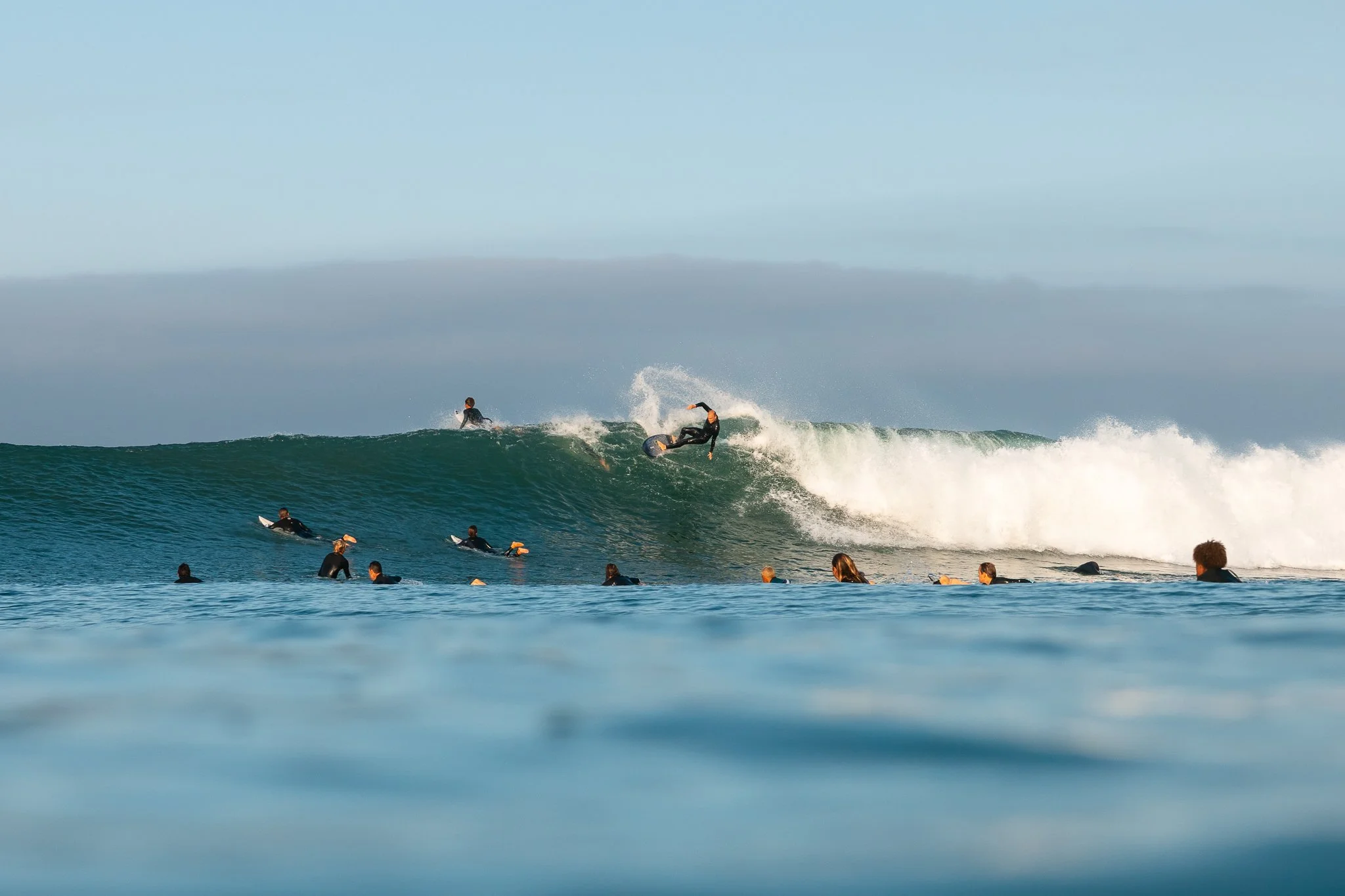 People surfing and swimming in the ocean with a large wave about to break.