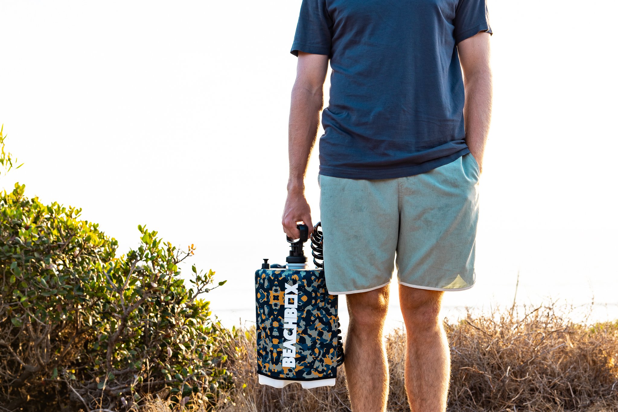 Person wearing a navy T-shirt and light gray shorts holding a hatch box in a natural outdoor setting.