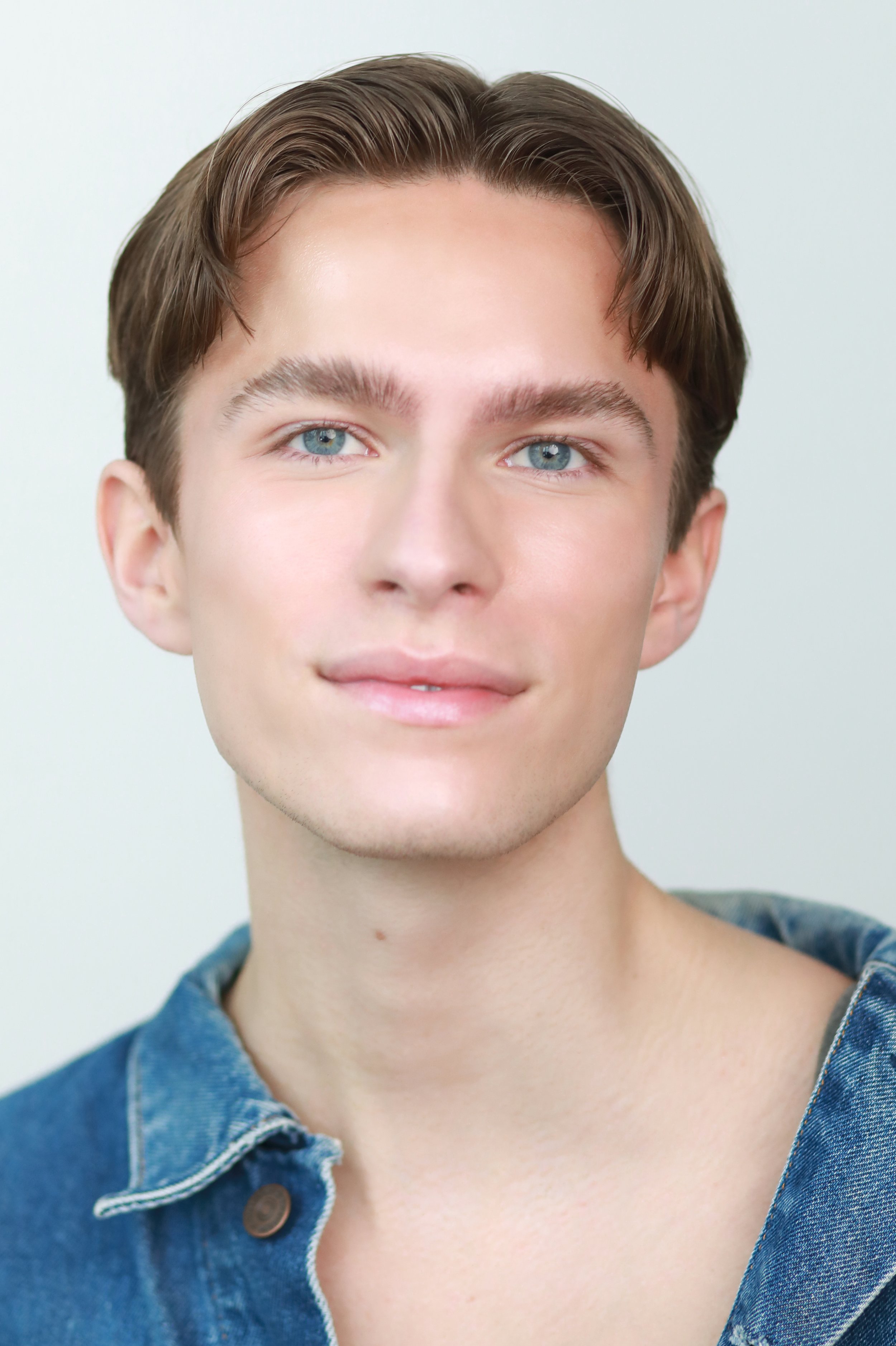Close-up of a young person's face with short brown hair, blue eyes, and wearing a blue denim jacket with a collar.