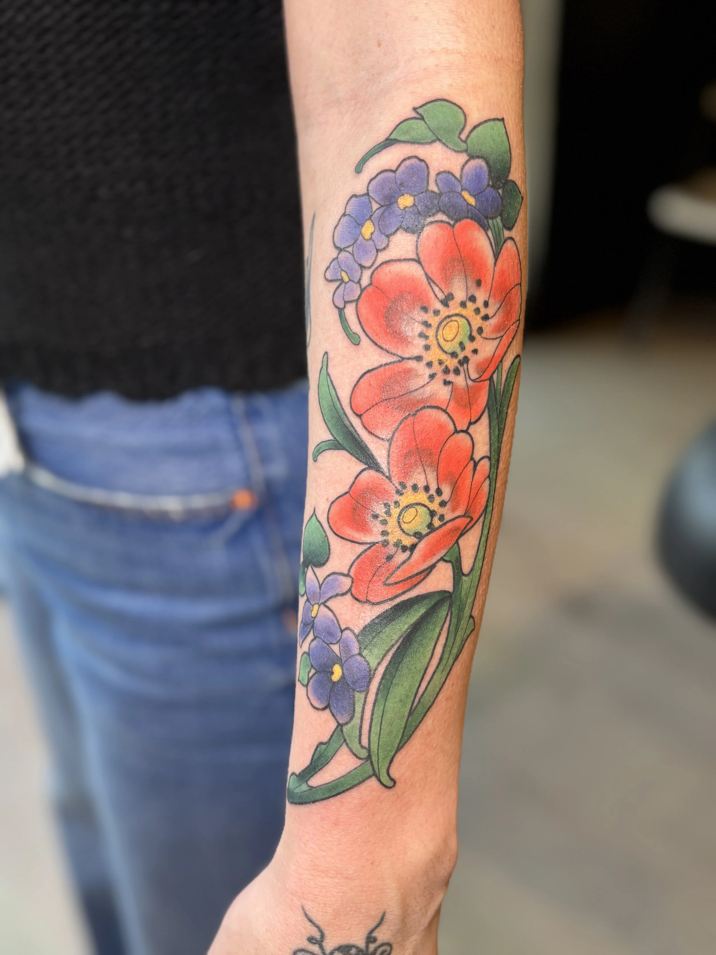 Colorful floral tattoo featuring red poppies and purple flowers on a person's forearm.