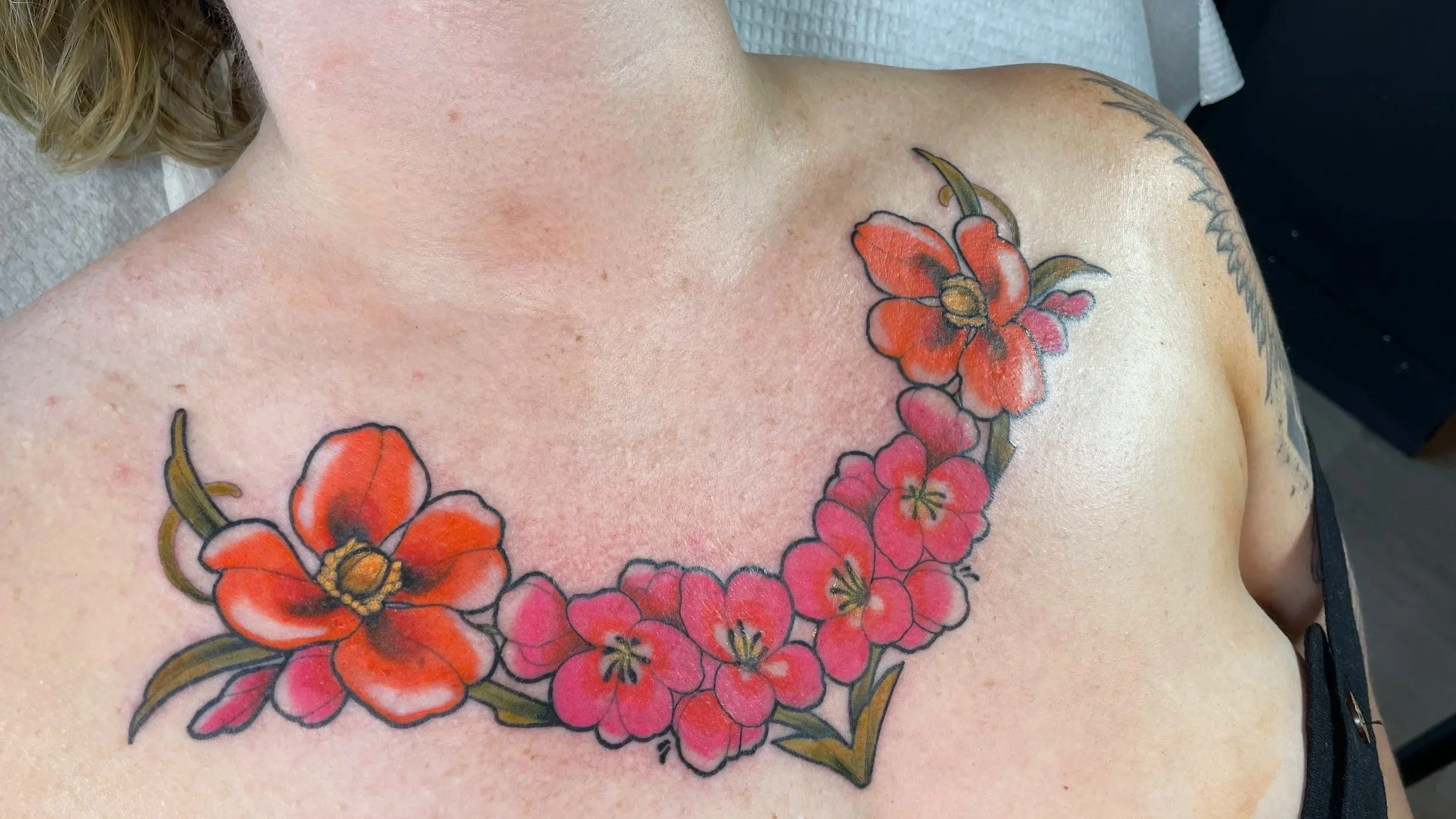 Colorful floral tattoo on woman's chest, featuring large orange and pink flowers with green leaves.