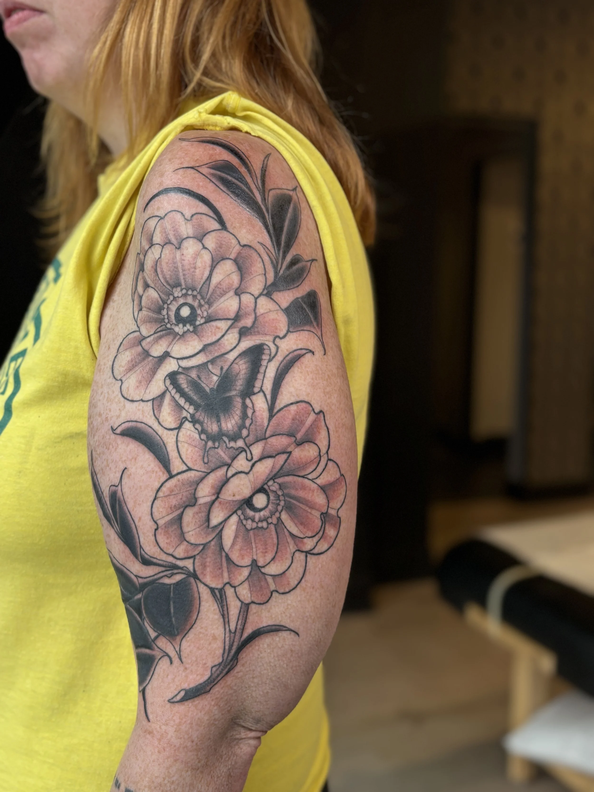 Tattoo of flowers and a butterfly on a person's upper arm.