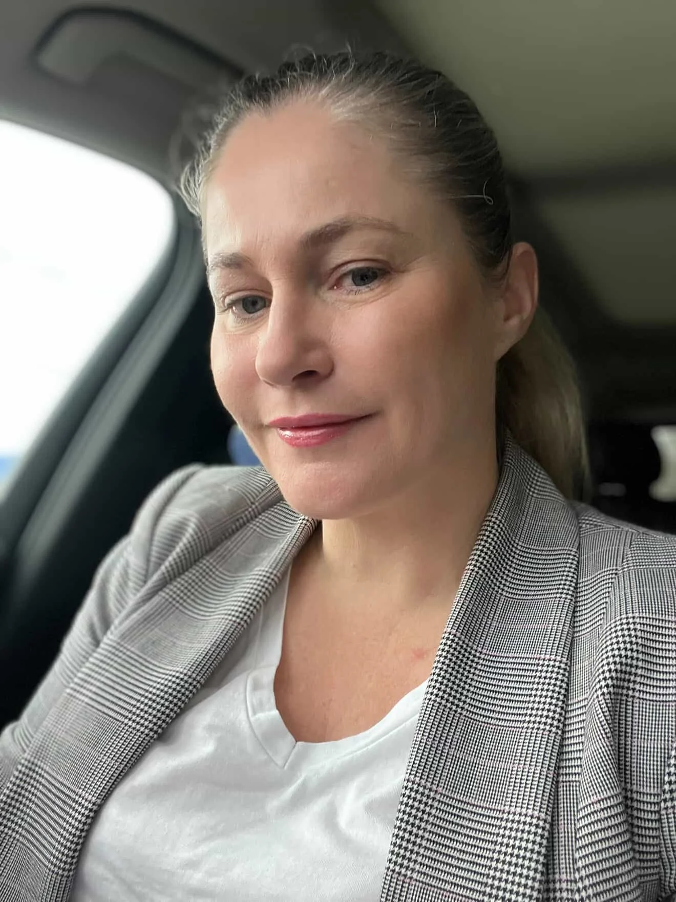 Christie also known as Birthing Generations sitting in a car wearing a grey checkered blazer smiling at the camera