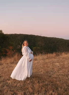 Rose from Mothered Doula, a pregnant woman in a white dress standing in a field at sunset.