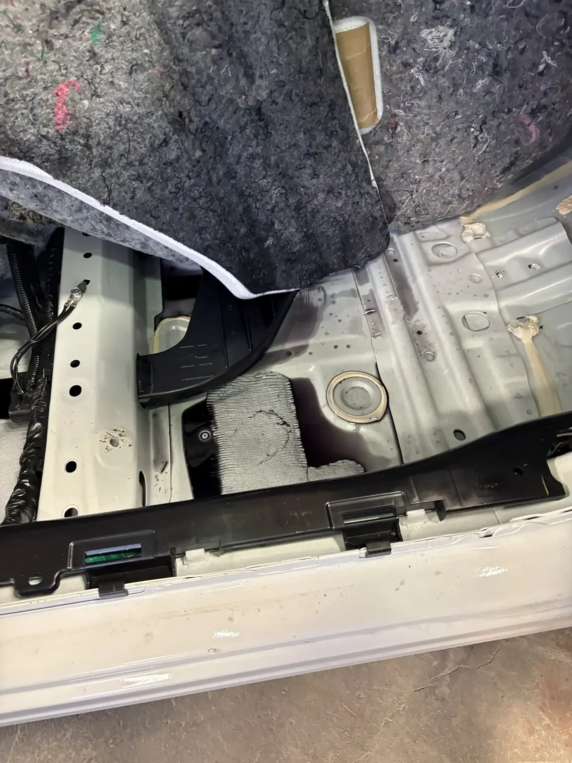 Chemical-soaked vehicle carpet underlay lifted above droplets of concentrated degreaser on the exposed floor