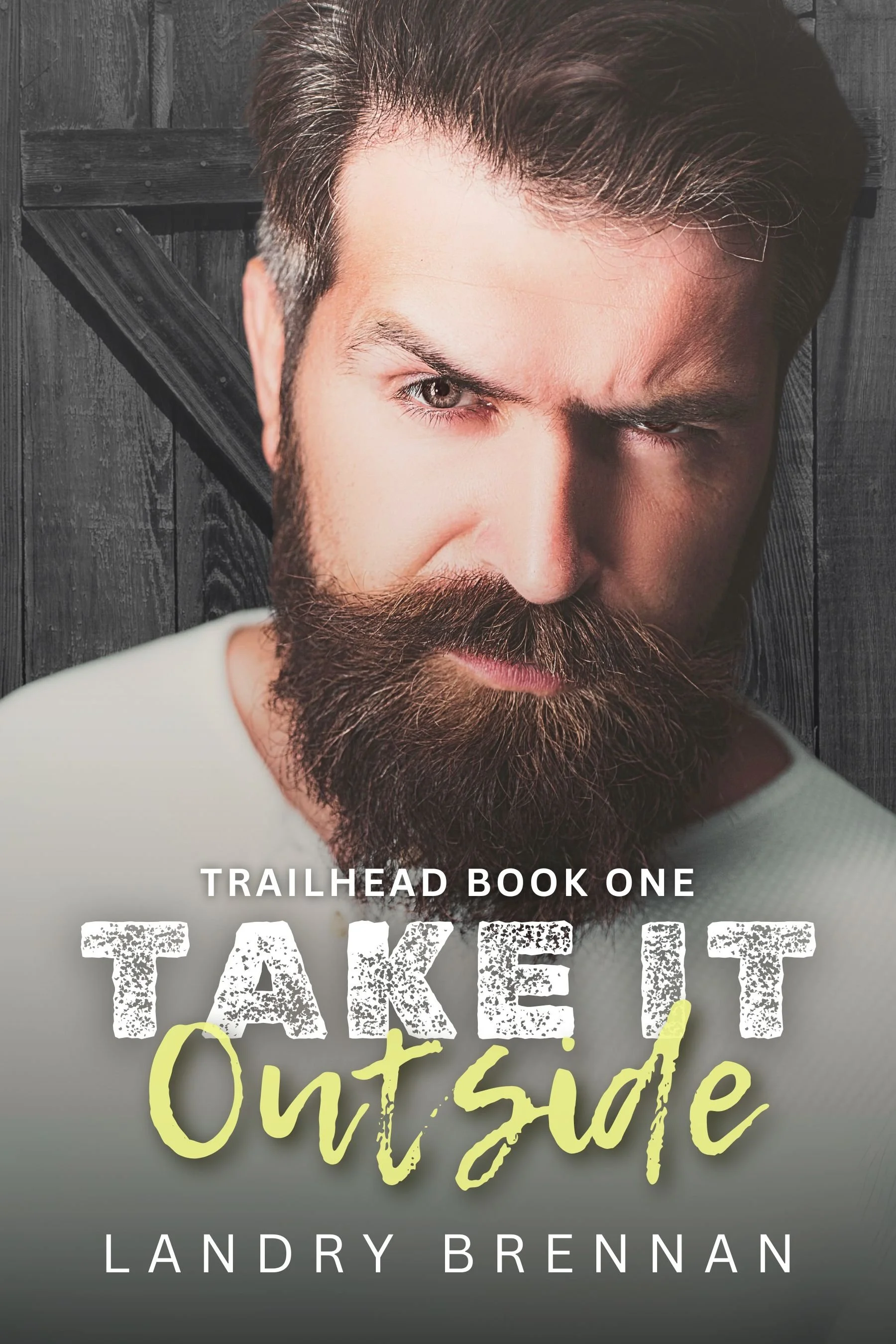 Close-up of a man with a thick beard and styled hair, winking at the camera, with a wooden background. Text overlay reads 'Trailhead Book One Take It Outside Landry Brennan.'