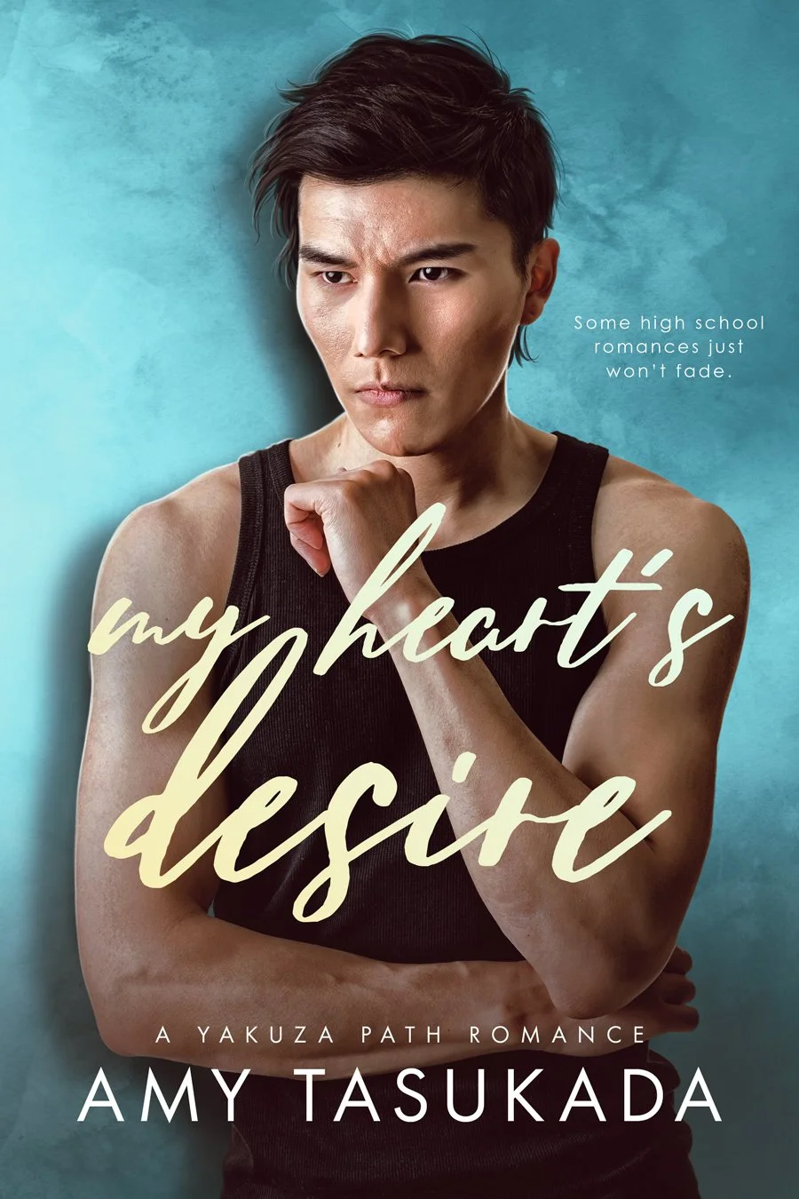 Cover of a book titled "My Heart's Desire" by Amy Tasukada. It features a young man with short dark hair, wearing a black tank top, holding his chin with a serious expression against a blue background.