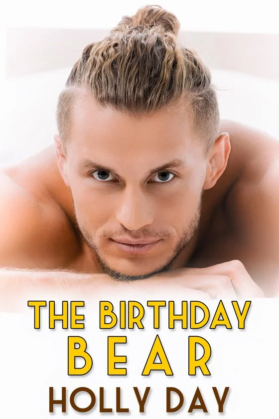 A shirtless man with styled blonde hair lying on a bed, looking directly at the camera, with overlay text that says "The Birthday Bear Holly Day."