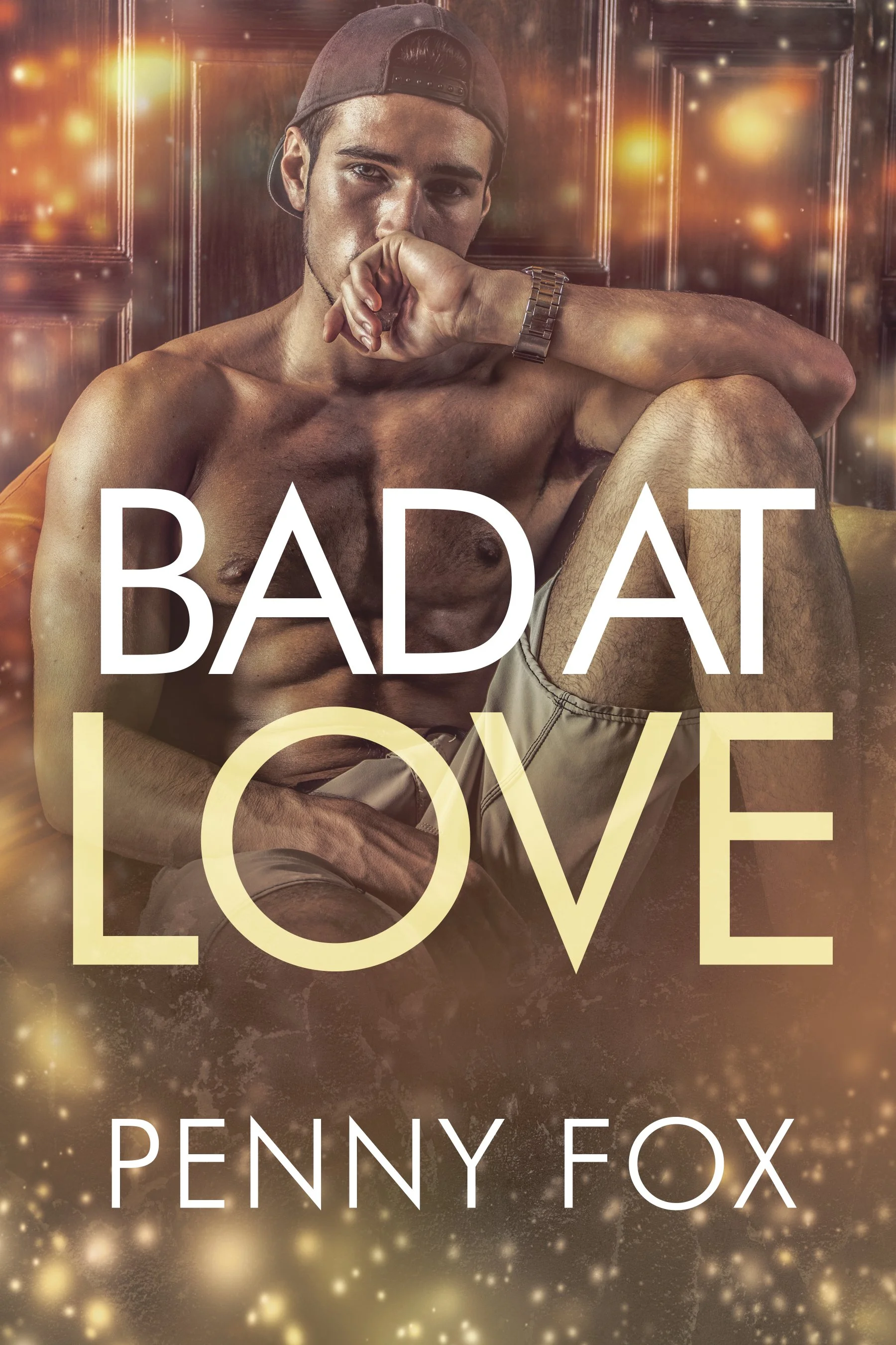 Book cover titled 'Bad At Love' by Penny Fox, featuring a shirtless young man with a cap sitting on a yellow couch, with a blurred background and glowing light effects.