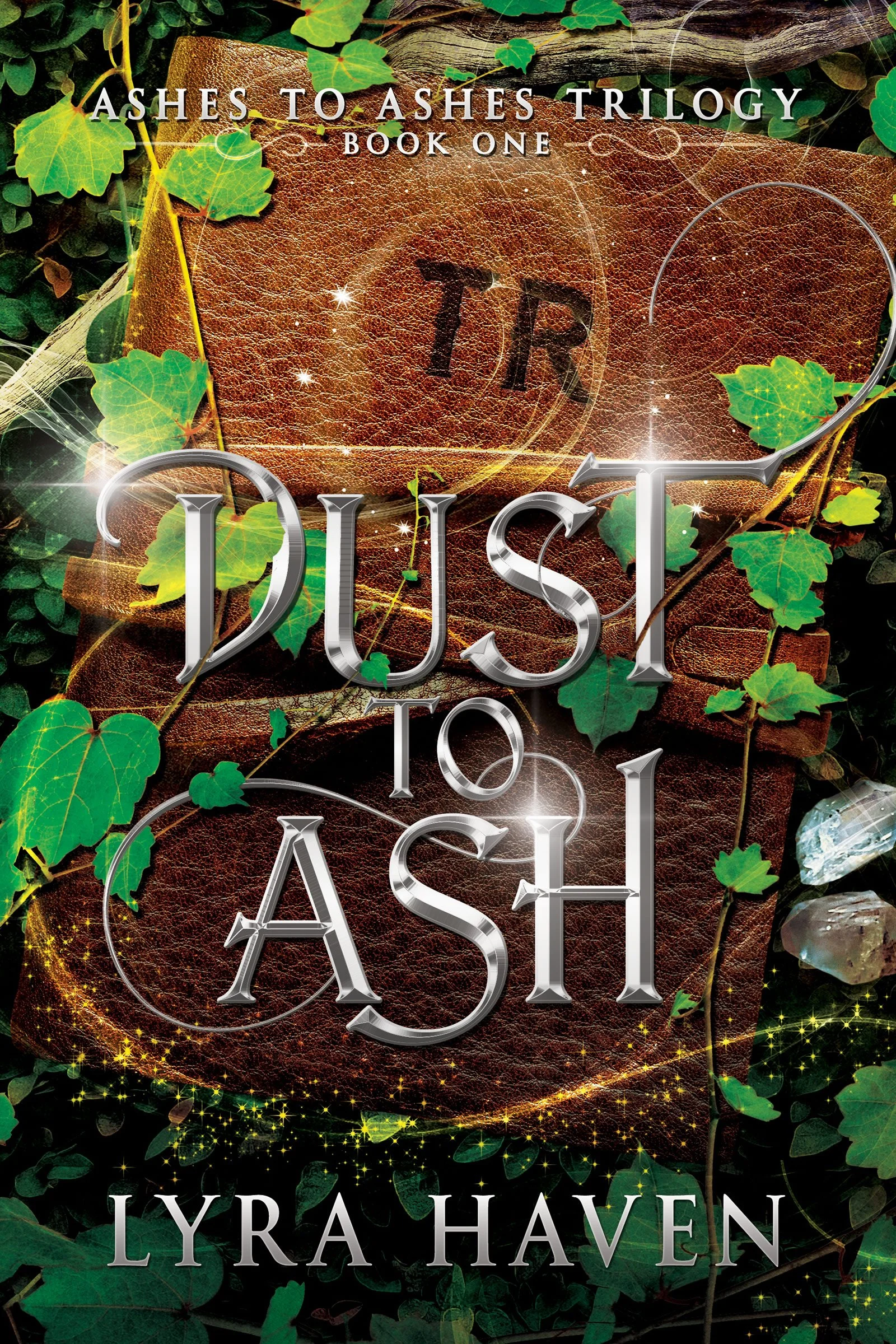 The book cover of 'Ashes to Ashes Trilogy Book One: Dust to Lyra Haven' features a brown leather-bound book with 'TR' stamped on the cover. Surrounding the book are green ivy leaves, sparkling golden lights, and a faint celestial glow. The title and author's name are displayed in silver metallic text over the image.