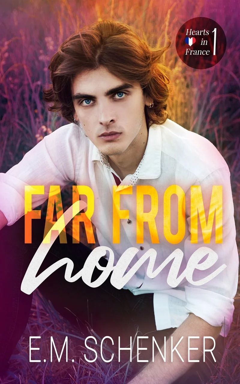 Book cover for 'Far From Home' by E.M. Schenker featuring a young man with blue eyes and brown hair, wearing a white shirt, sitting in colorful tall grass at sunset.