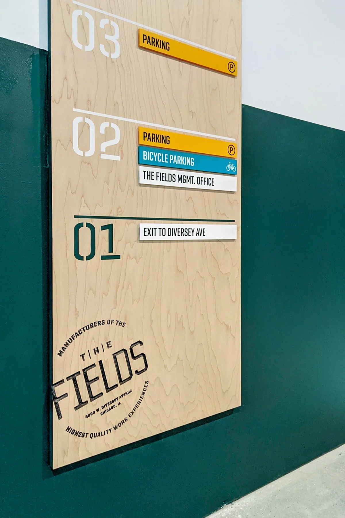 A directory sign with four levels. Level 3 has parking, Level 2 has parking, bicycle parking, and office. Level 1 has an exit to Diversey Avenue. The sign is attached to a wooden panel with a logo of The Fields restaurant at the bottom.