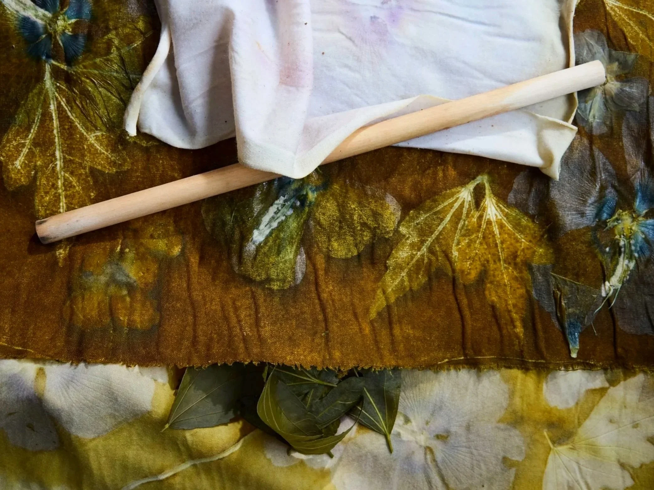 A table covered with autumn leaves and fabric, a wooden stick, and cloth bundle.