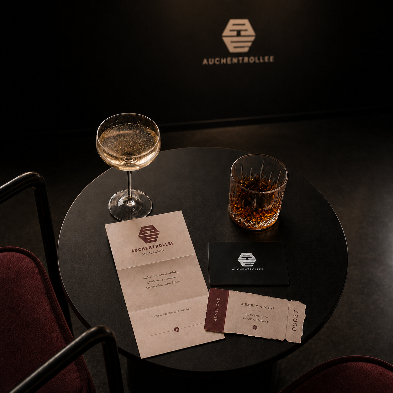 A black round table with two drinks, a member invitation letter, and a member access ticket, with the Auchentrolleye logo on a backdrop behind the table.