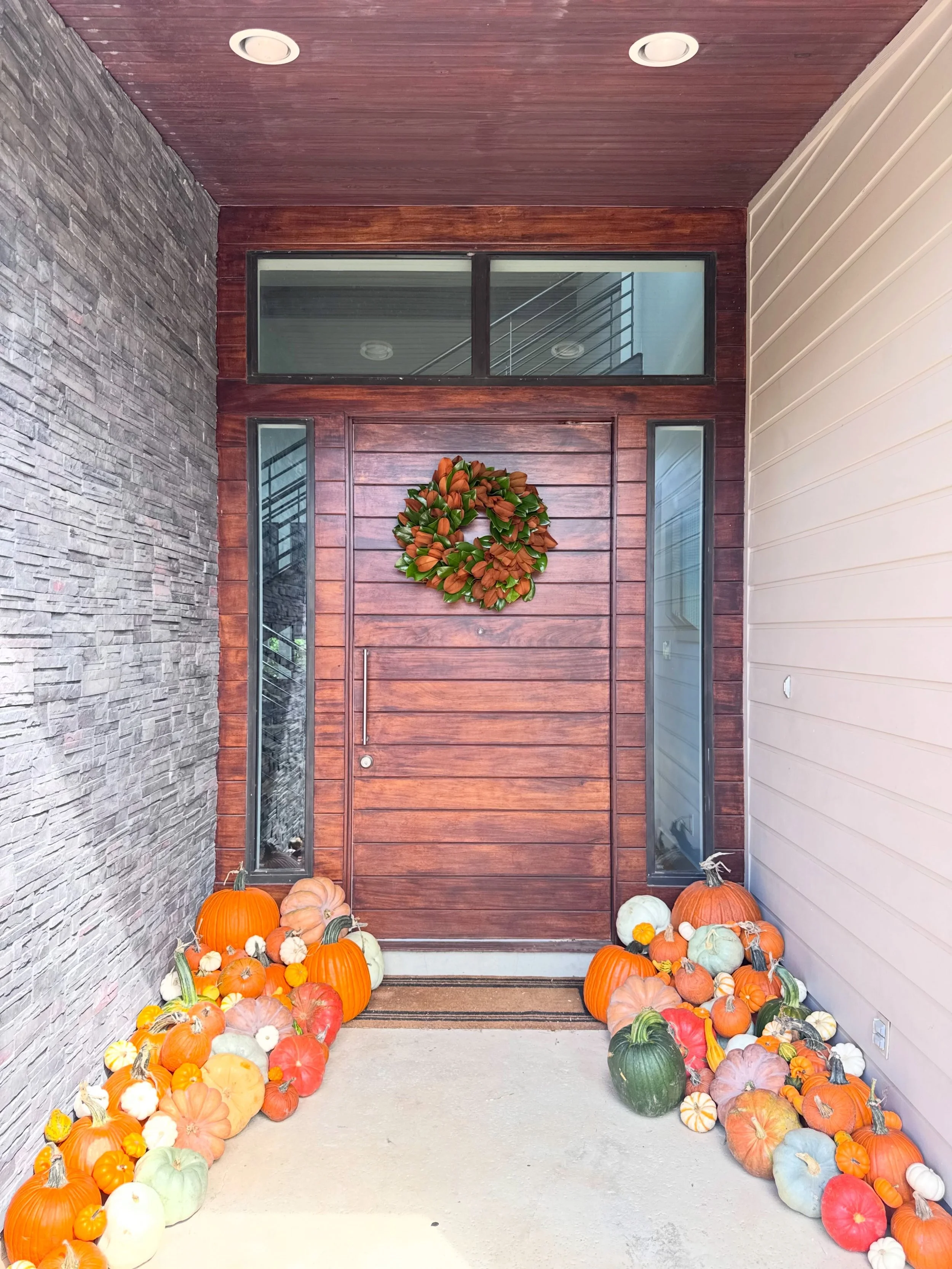 The finishing touch to a pumpkin-filled porch. 🍂 Our magnolia wreath brings rich greenery and warm tones to the front door, tying the whole fall look together with @htandco.1