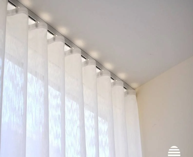 Close-up of white sheer curtains hanging from a ceiling-mounted curtain track, with soft natural light filtering through.