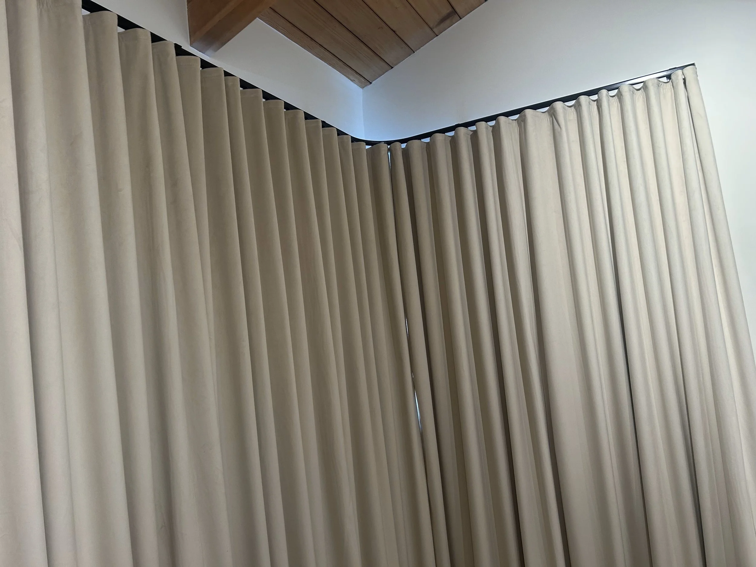 Light-colored curtains hanging in a room with a wooden ceiling.