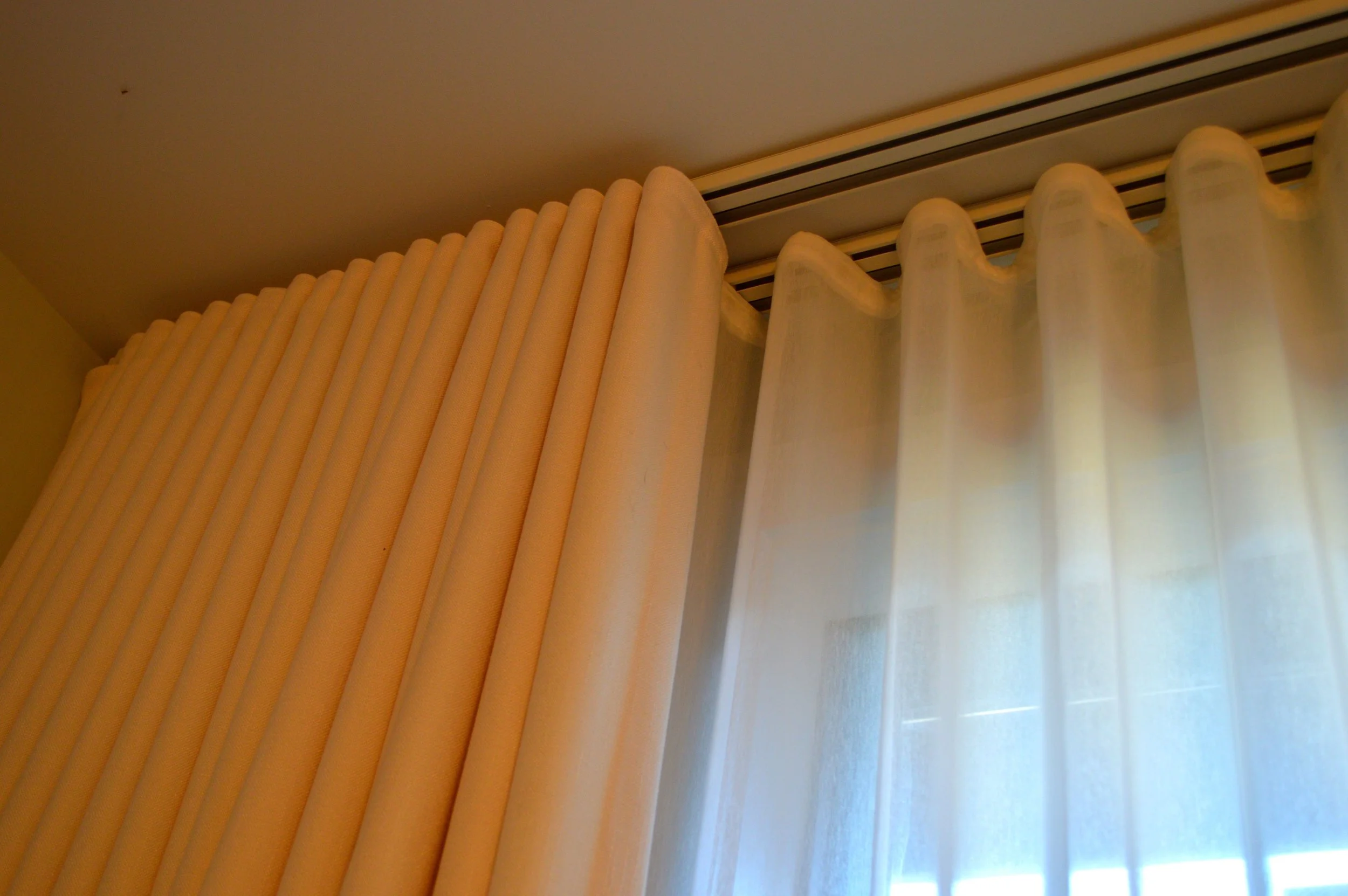 Cream-colored curtains with a sheer white curtain behind them hanging in front of a window.