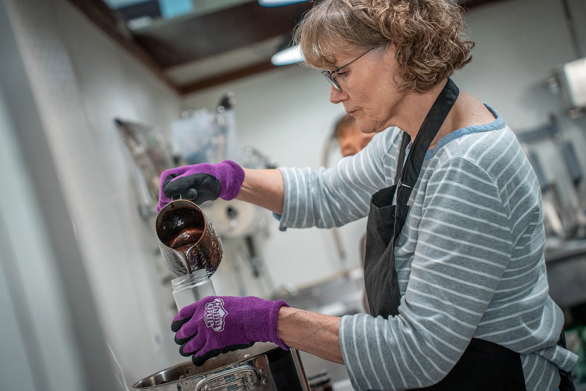 A woman pours chocolate sauce into an empty bottle.