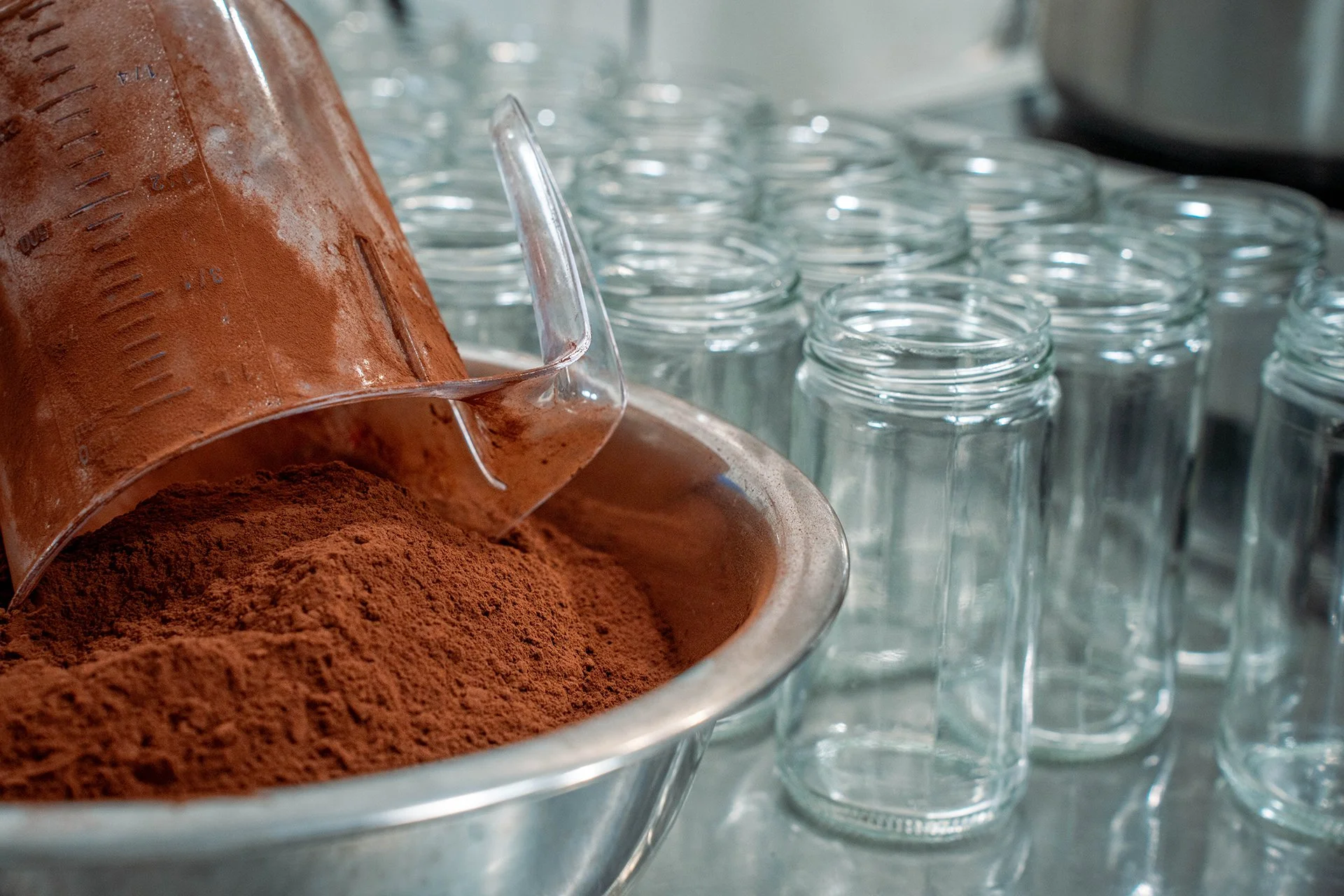 A measuring cup upside down in a bowl of cocoa powder, surrounded by empty bottles.