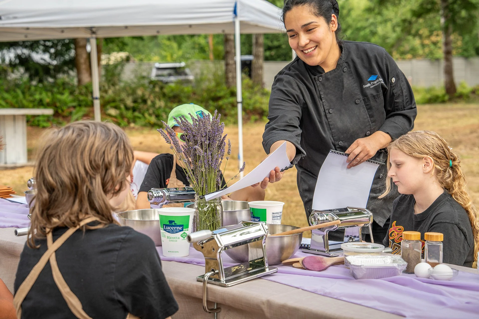 A woman chef hands a recipe to a student taking her cooking class.