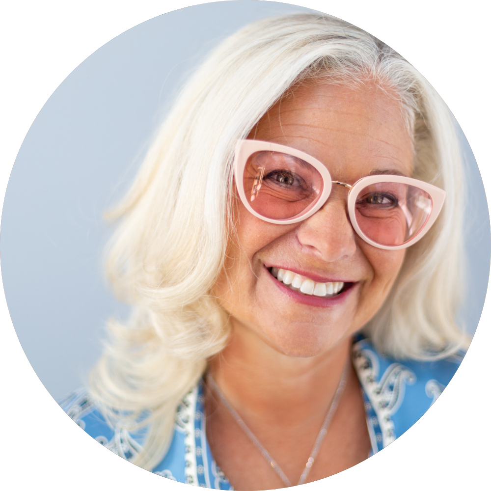 Shana Schwartz smiling in pink sunglasses and a blue patterned blouse.