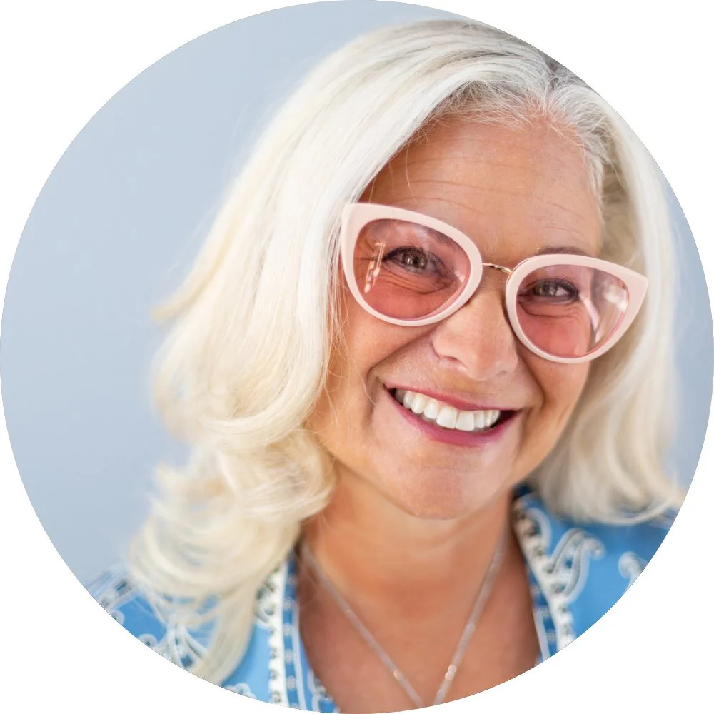 Shana Schwartz smiling in pink sunglasses and a blue patterned blouse.