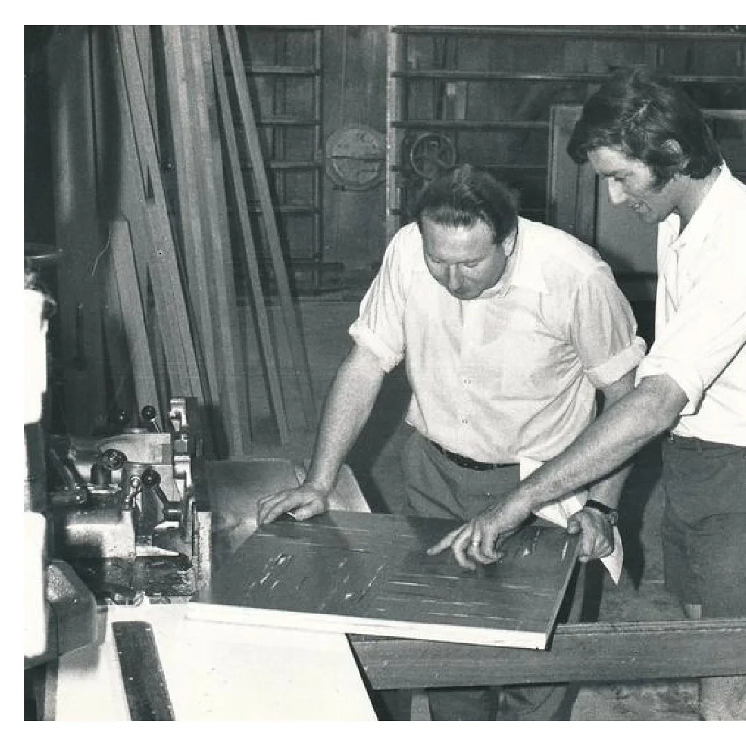 Two men working together in a woodworking workshop, examining a wooden board.