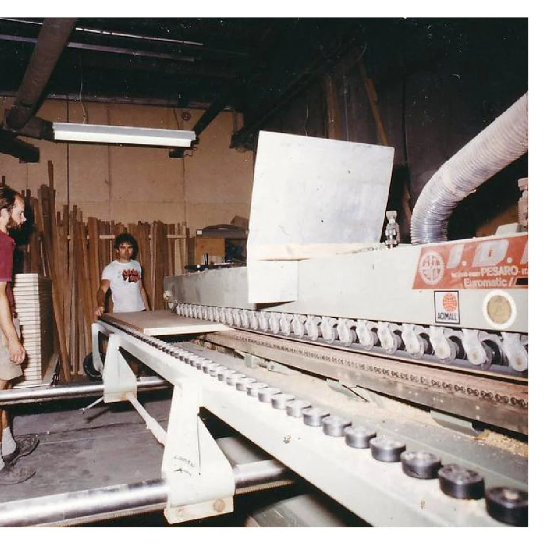 A woodworking workshop with two people standing near a large CNC machine, surrounded by wooden planks.