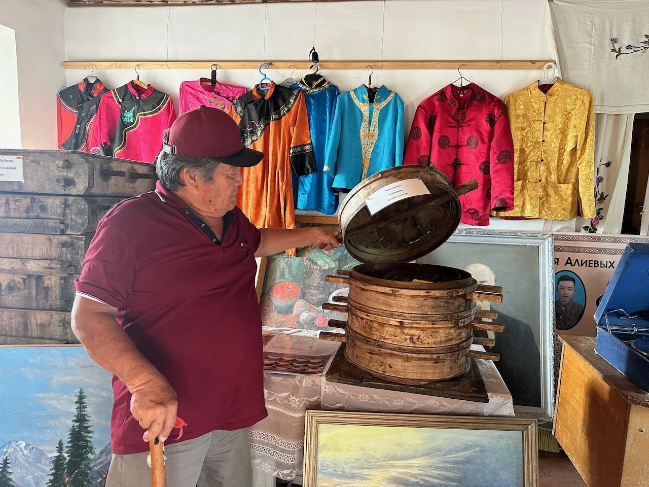  The docent showing us bamboo steamers used to make 包子 and 饅頭. You can seem some of the traditional clothing in the background. Paintings in the foreground are painted by artists from the village. 