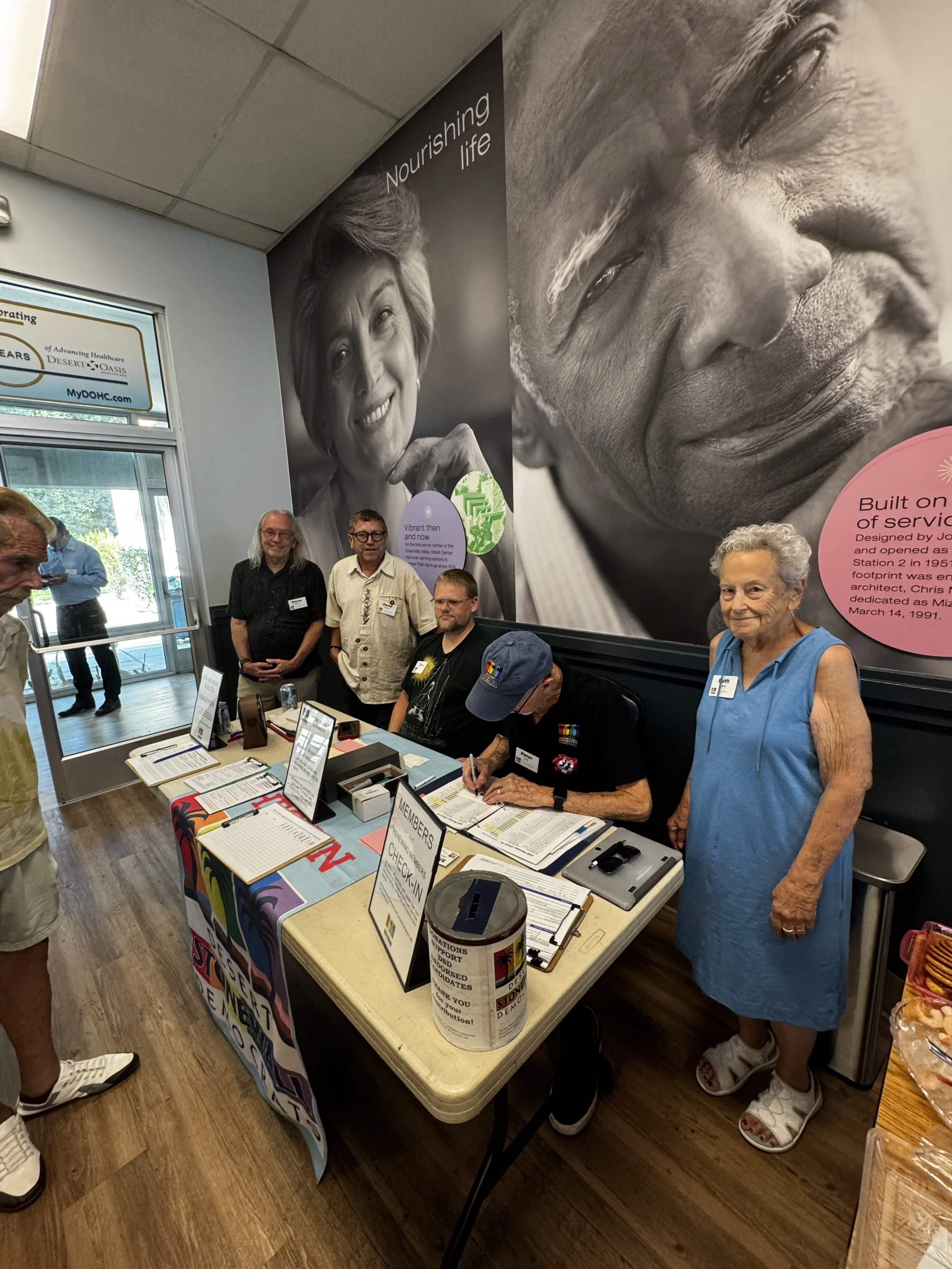 People gather around a registration table at an indoor event, with a large black and white mural of two faces and the words 'Nourishing life' in the background.