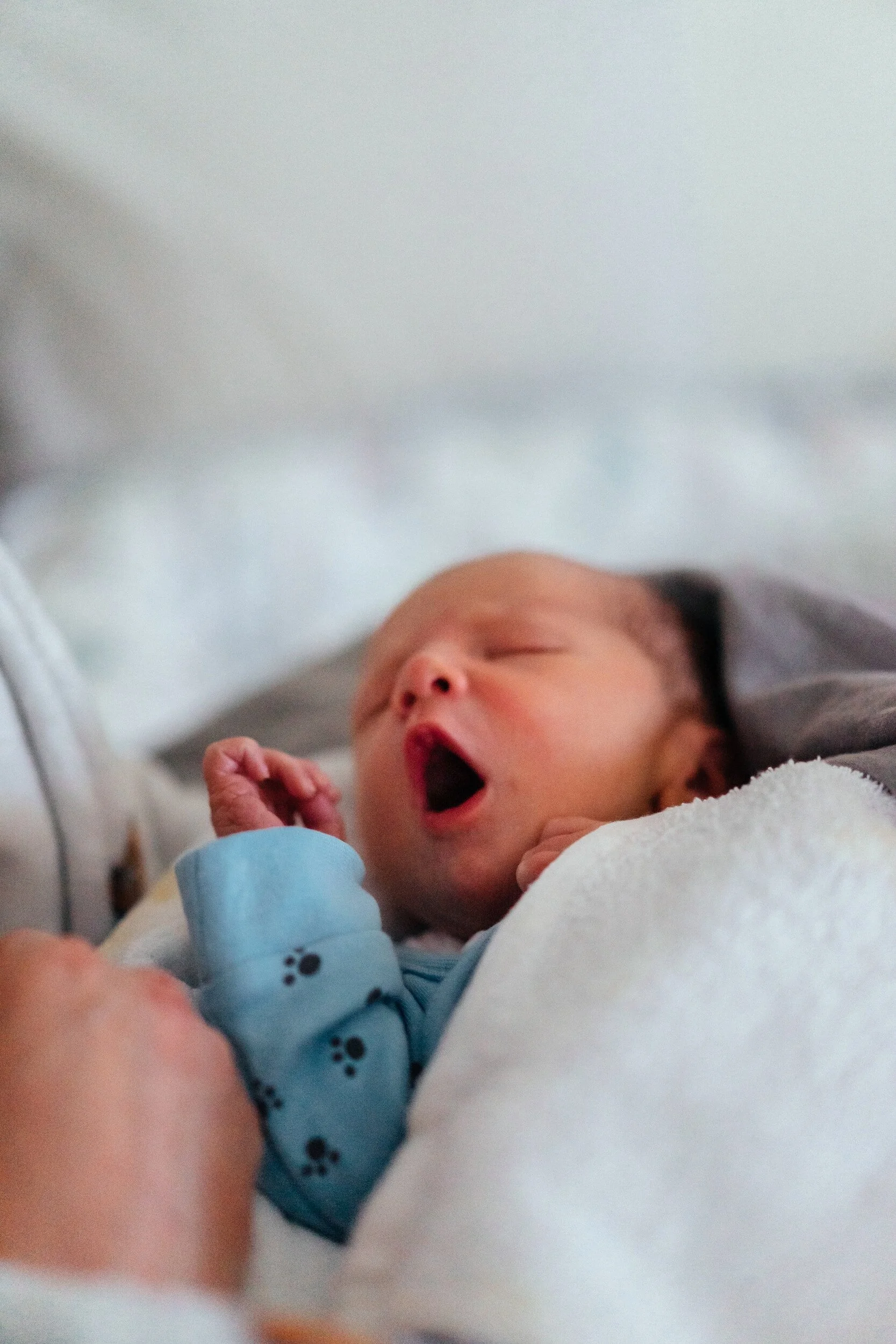 A newborn baby yawning while being held by an adult.