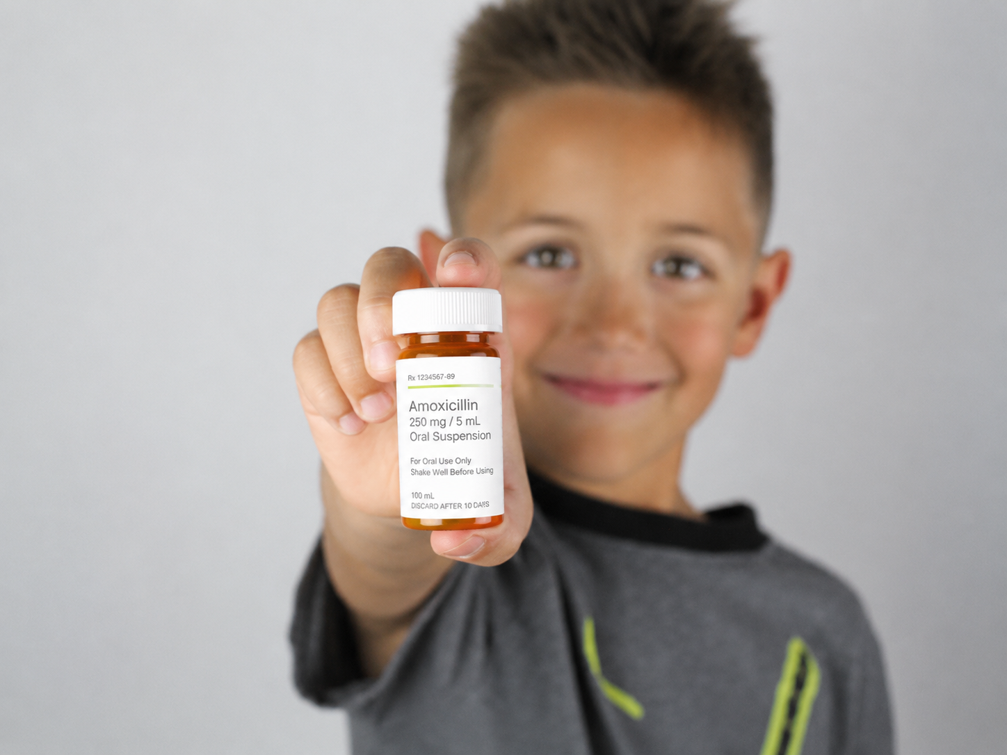 Small clear plastic bottle with pink liquid medication in the foreground, with several blurry brown medicine bottles in the background.