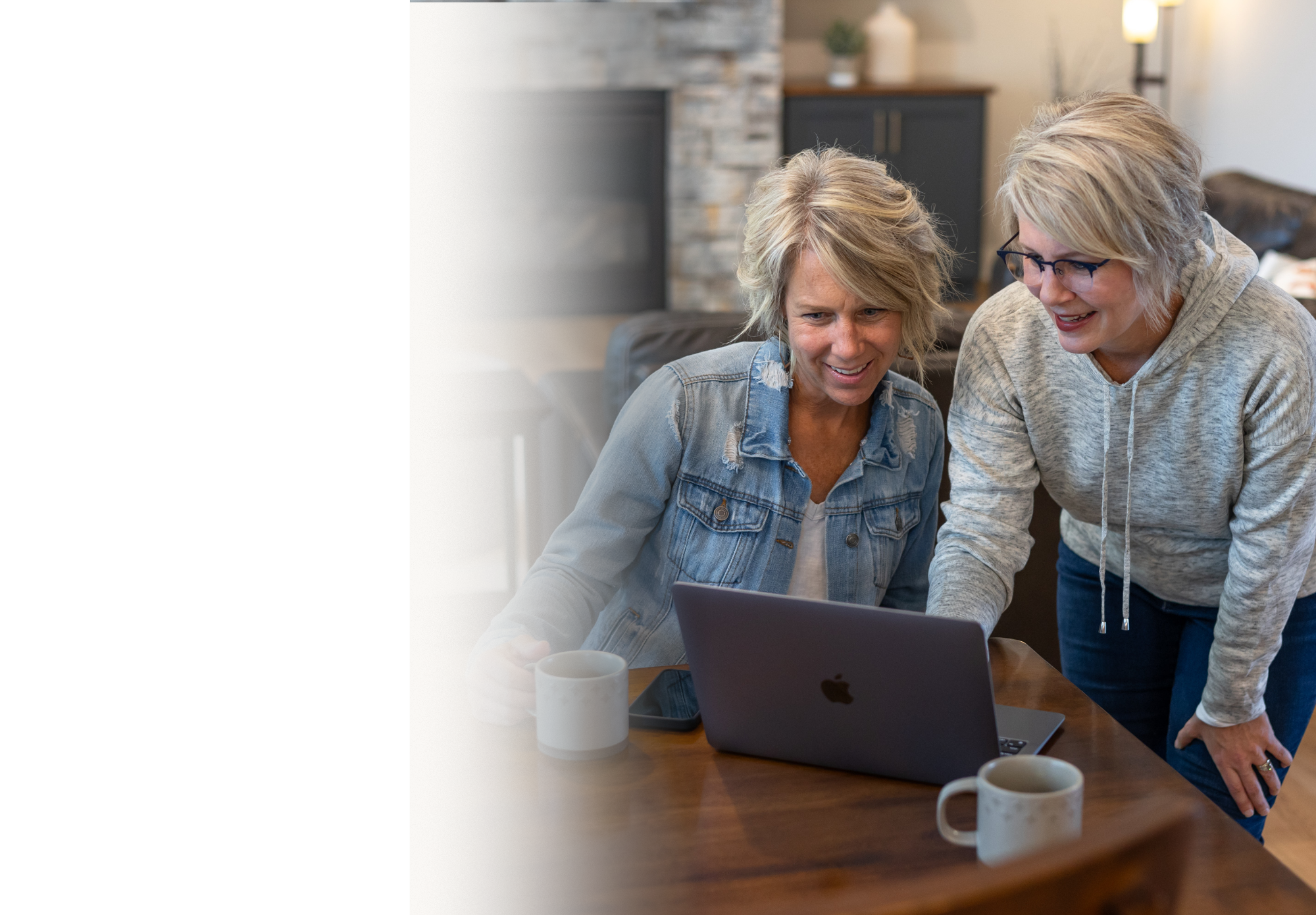 Heidi Zwart and a client looking at a laptop together and smiling while standing in a cozy, well-lit living room.