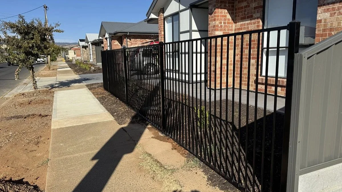 View of new brick houses with metal fences and a sidewalk on a sunny day.
