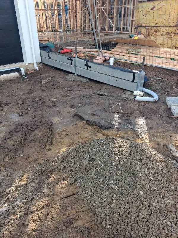 Construction site with a partially built raised garden bed and a pile of gravel in the foreground.